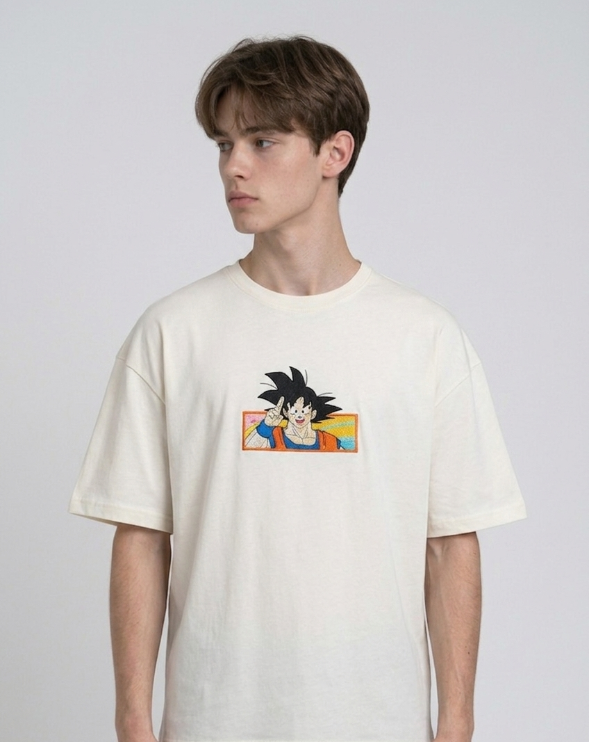 Front view of a male model with middle-parted brown hair wearing an Anetoonz dark grey mineral wash oversized t-shirt featuring a detailed, embroidered graphic of Son Goku from Dragon Ball Z giving a peace sign within a colorful framed background.