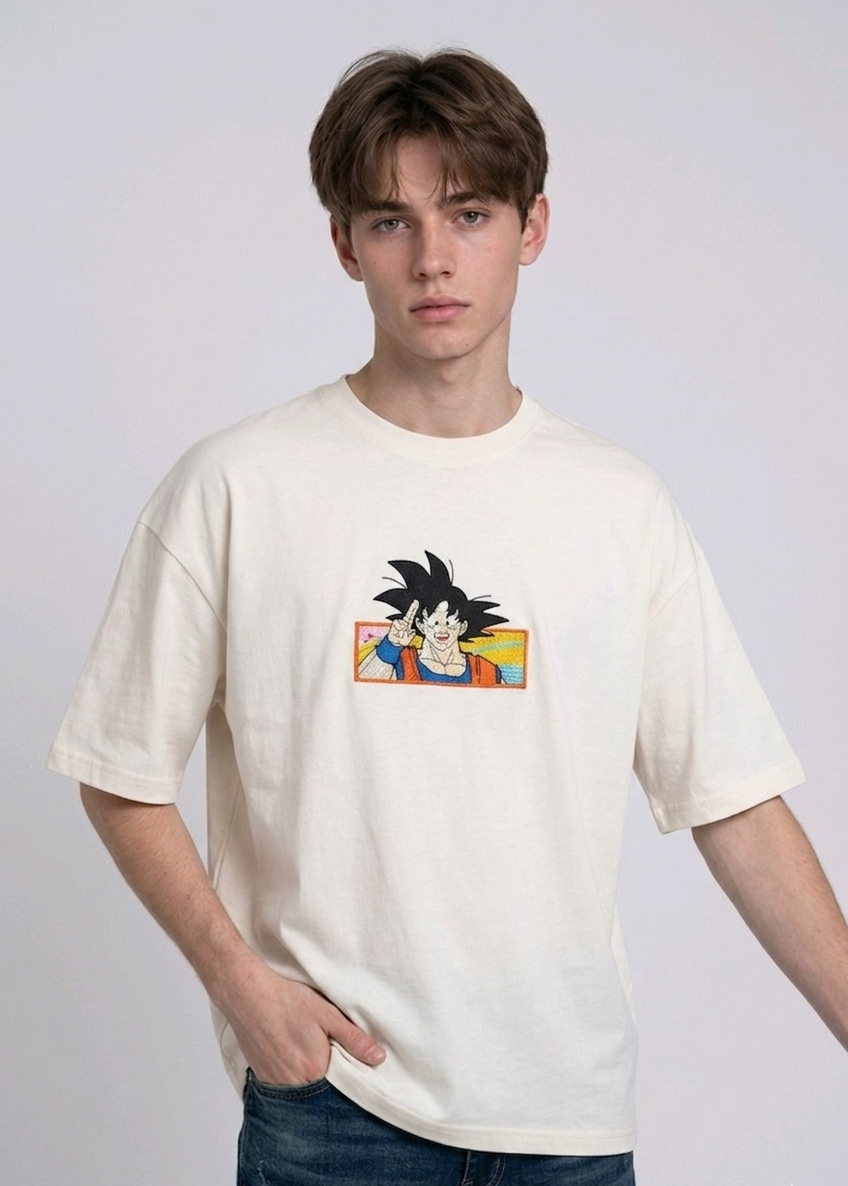 Front view of a male model with middle-parted brown hair wearing an Anetoonz dark grey mineral wash oversized t-shirt featuring a detailed, embroidered graphic of Son Goku from Dragon Ball Z giving a peace sign within a colorful framed background.