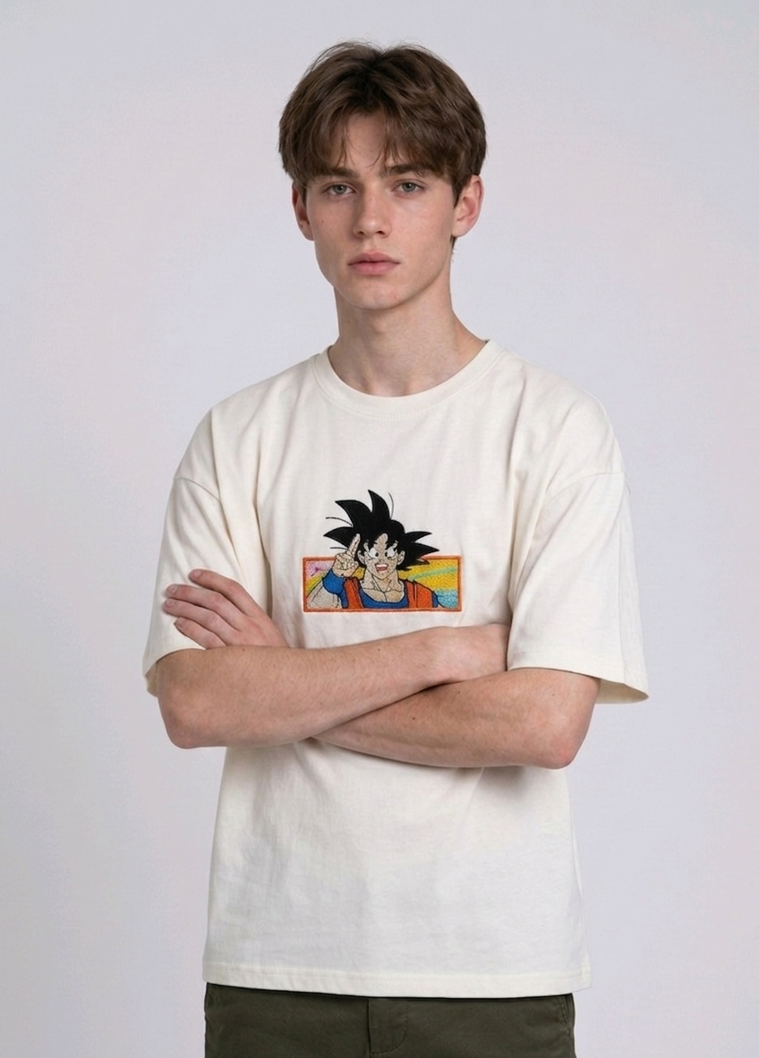 Front view of a male model with middle-parted brown hair wearing an Anetoonz dark grey mineral wash oversized t-shirt featuring a detailed, embroidered graphic of Son Goku from Dragon Ball Z giving a peace sign within a colorful framed background.