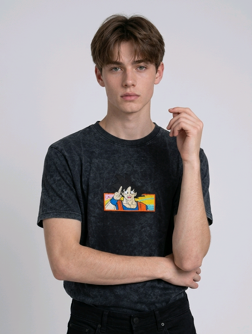 Front view of a male model with middle-parted brown hair wearing an Anetoonz dark grey mineral wash oversized t-shirt featuring a detailed, embroidered graphic of Son Goku from Dragon Ball Z giving a peace sign within a colorful framed background.