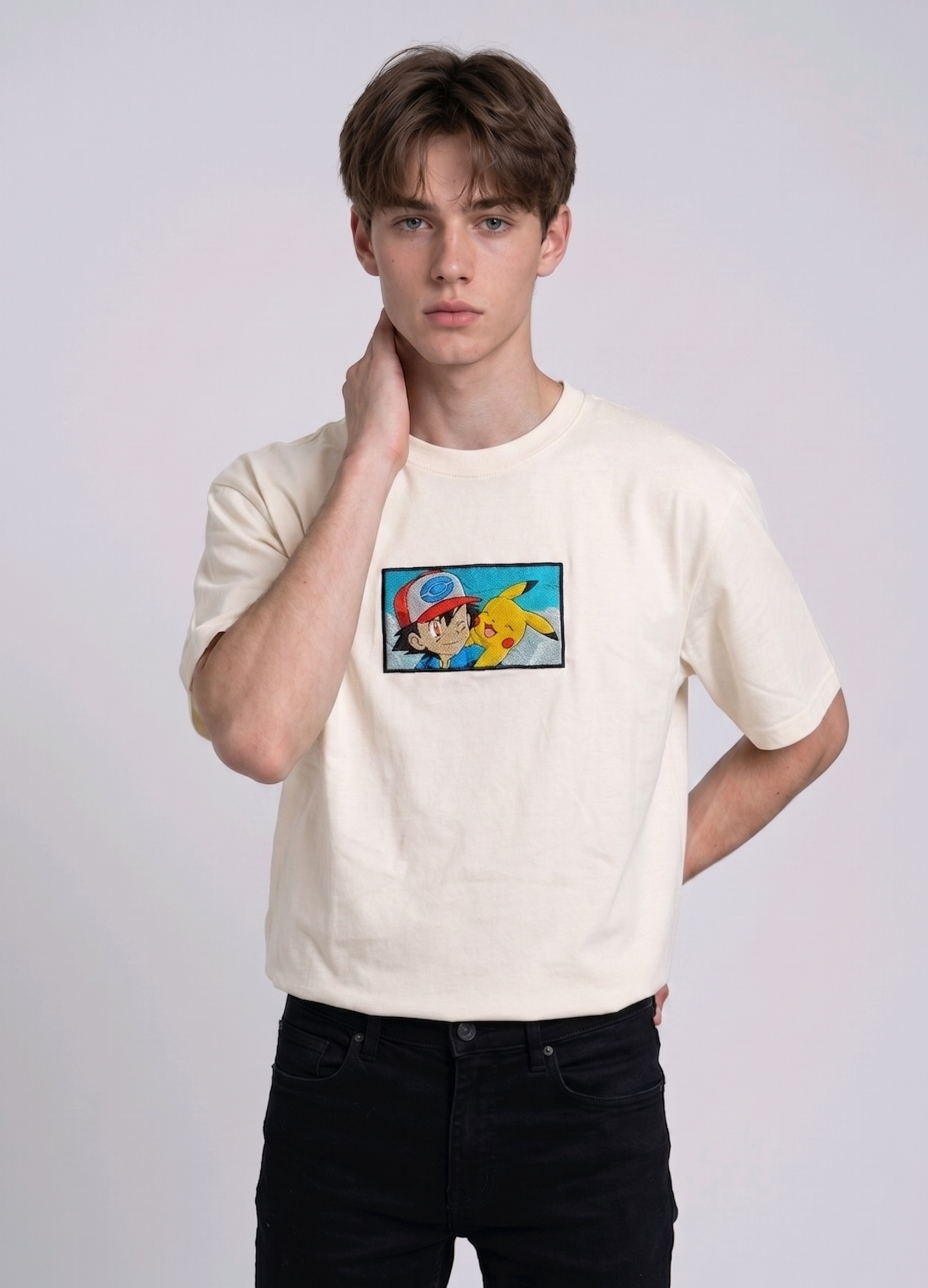 He is wearing heavyweight cotton t-shirt with a detailed, colorful embroidered patch on the chest featuring anime characters Ash Ketchum (winking) and Pikachu.