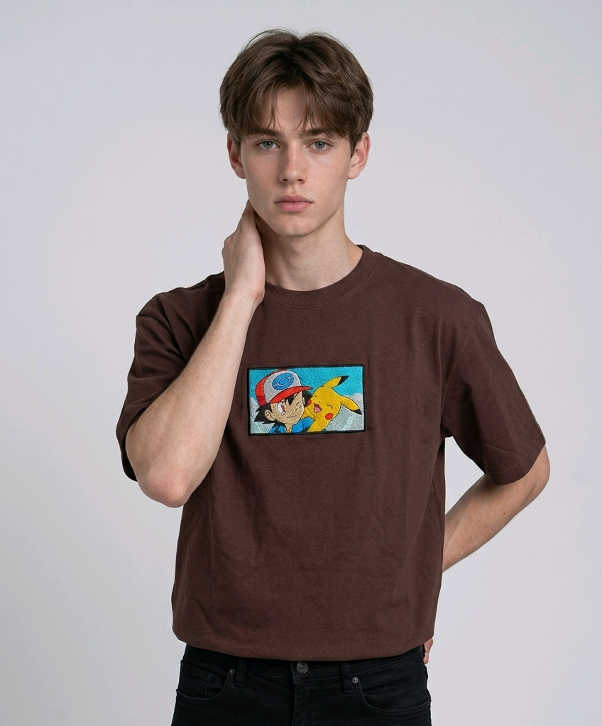 He is wearing , heavyweight cotton t-shirt with a detailed, colorful embroidered patch on the chest featuring anime characters Ash Ketchum (winking) and Pikachu.