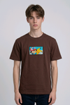 He is wearing , heavyweight cotton t-shirt with a detailed, colorful embroidered patch on the chest featuring anime characters Ash Ketchum (winking) and Pikachu.