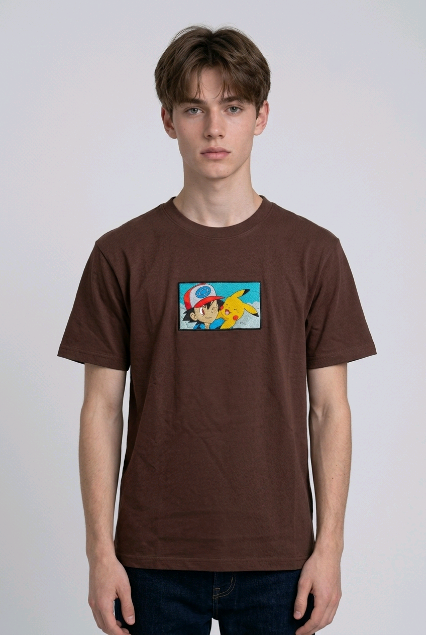 He is wearing , heavyweight cotton t-shirt with a detailed, colorful embroidered patch on the chest featuring anime characters Ash Ketchum (winking) and Pikachu.