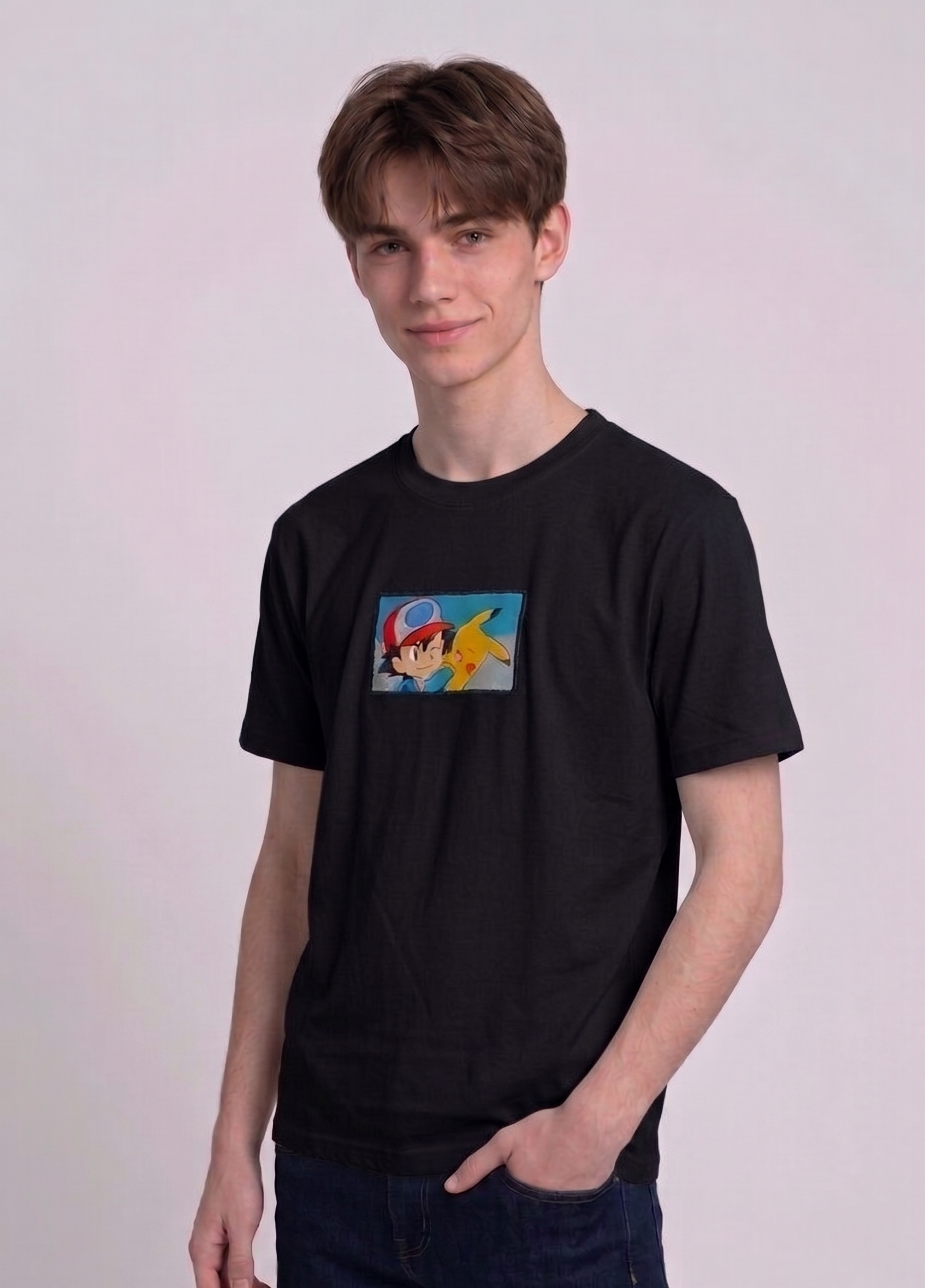 He is wearing a dark, heavyweight cotton t-shirt with a detailed, colorful embroidered patch on the chest featuring anime characters Ash Ketchum (winking) and Pikachu.