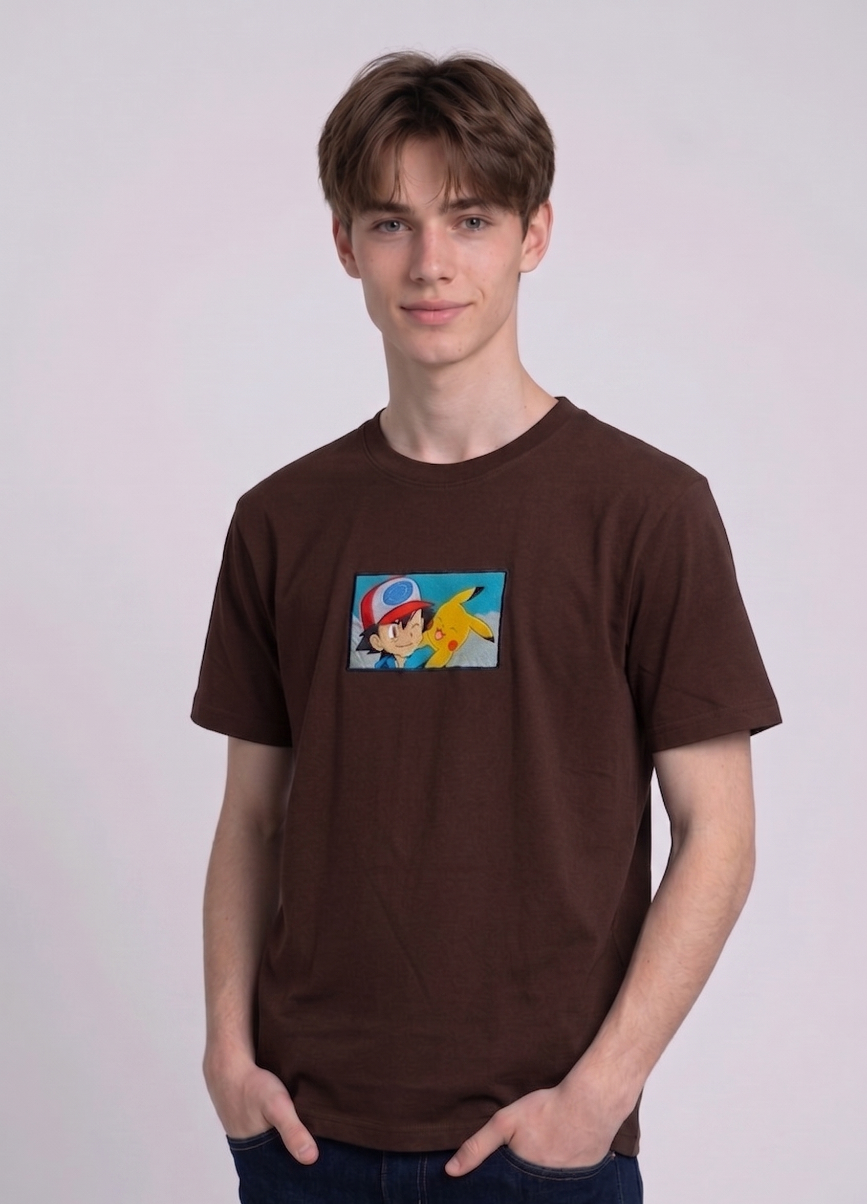 He is wearing , heavyweight cotton t-shirt with a detailed, colorful embroidered patch on the chest featuring anime characters Ash Ketchum (winking) and Pikachu.