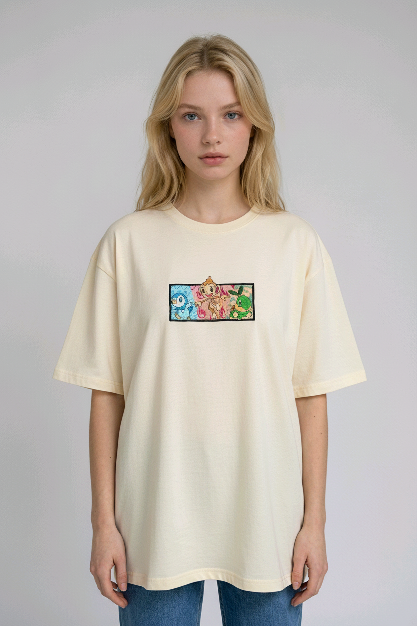 A young woman with wavy blonde hair standing against a plain grey studio background. She has her arms crossed and is wearing a white crew-neck t-shirt.

