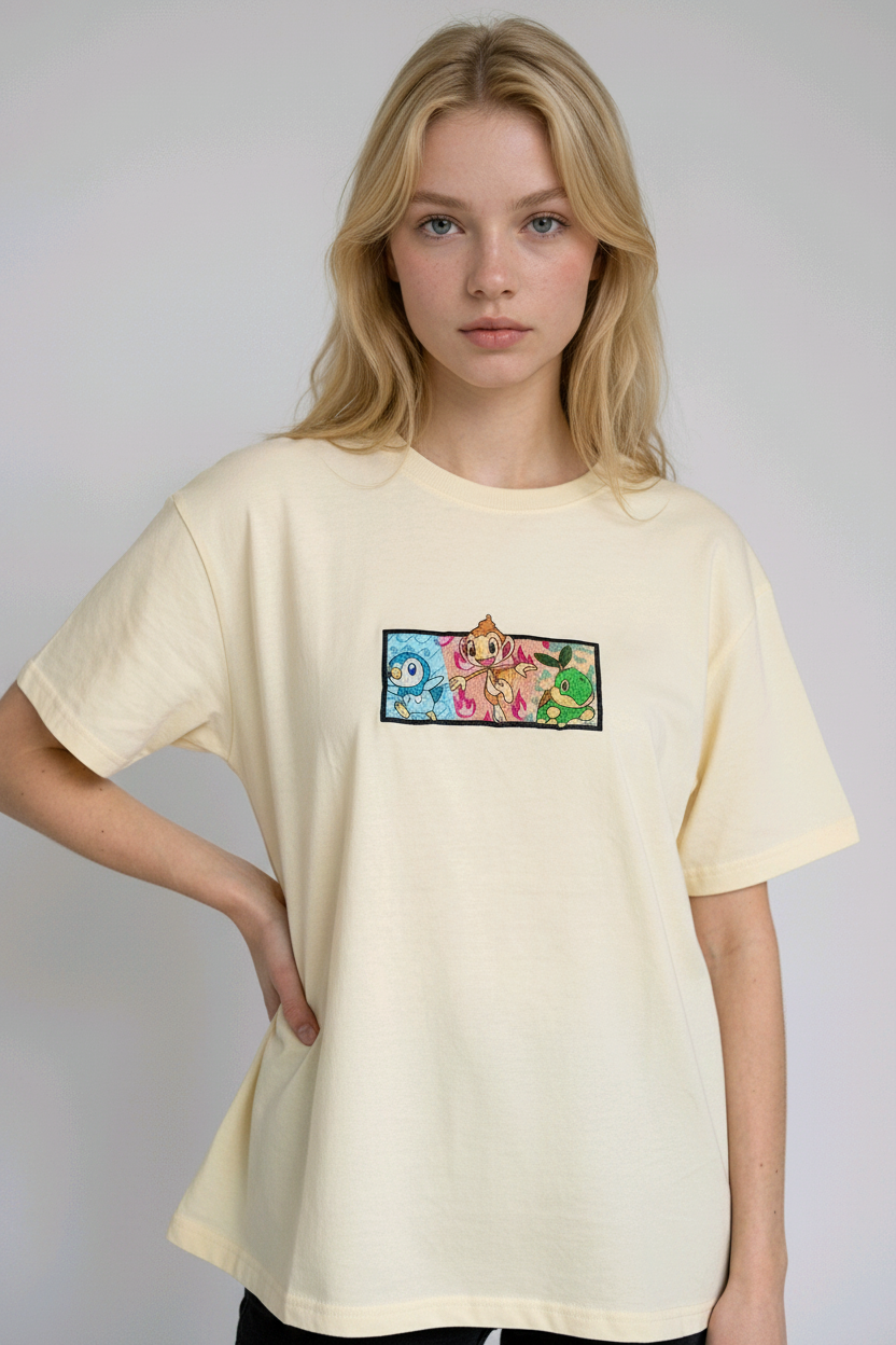 A young woman with wavy blonde hair standing against a plain grey studio background. She has her arms crossed and is wearing a white crew-neck t-shirt.

