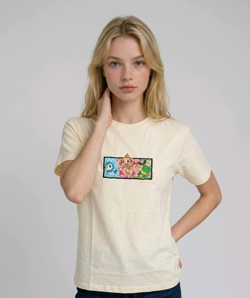 A young woman with wavy blonde hair standing against a plain grey studio background. She has her arms crossed and is wearing a white crew-neck t-shirt.

