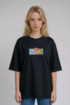 A young woman with wavy blonde hair standing against a plain grey studio background. She has her arms crossed and is wearing a black crew-neck t-shirt.
