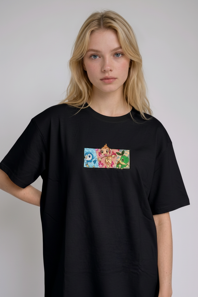 A young woman with wavy blonde hair standing against a plain grey studio background. She has her arms crossed and is wearing a black crew-neck t-shirt.
