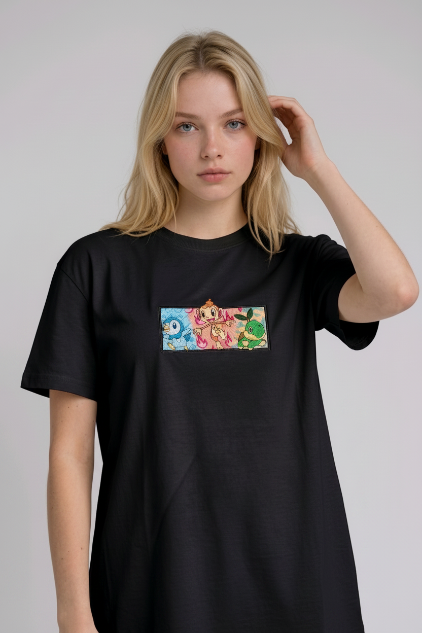 A young woman with wavy blonde hair standing against a plain grey studio background. She has her arms crossed and is wearing a black crew-neck t-shirt.
