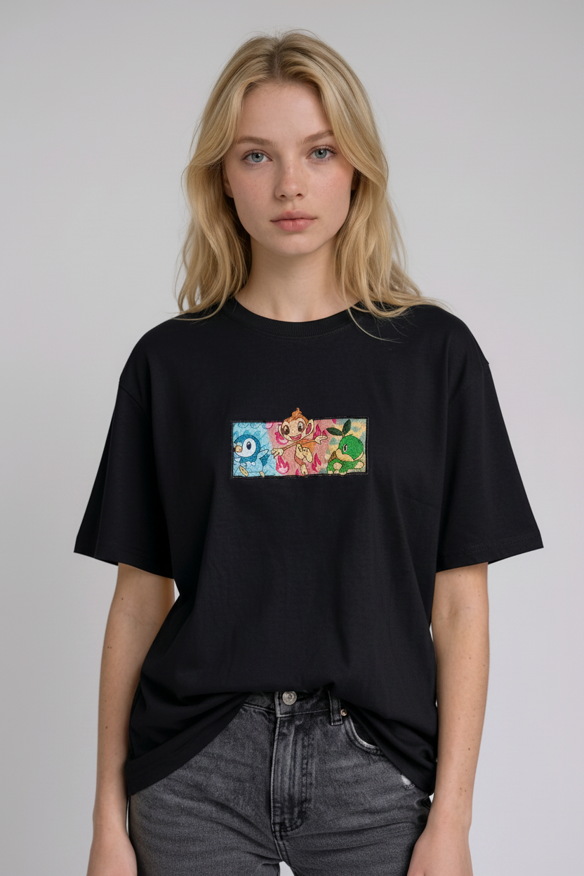 A young woman with wavy blonde hair standing against a plain grey studio background. She has her arms crossed and is wearing a black crew-neck t-shirt.
