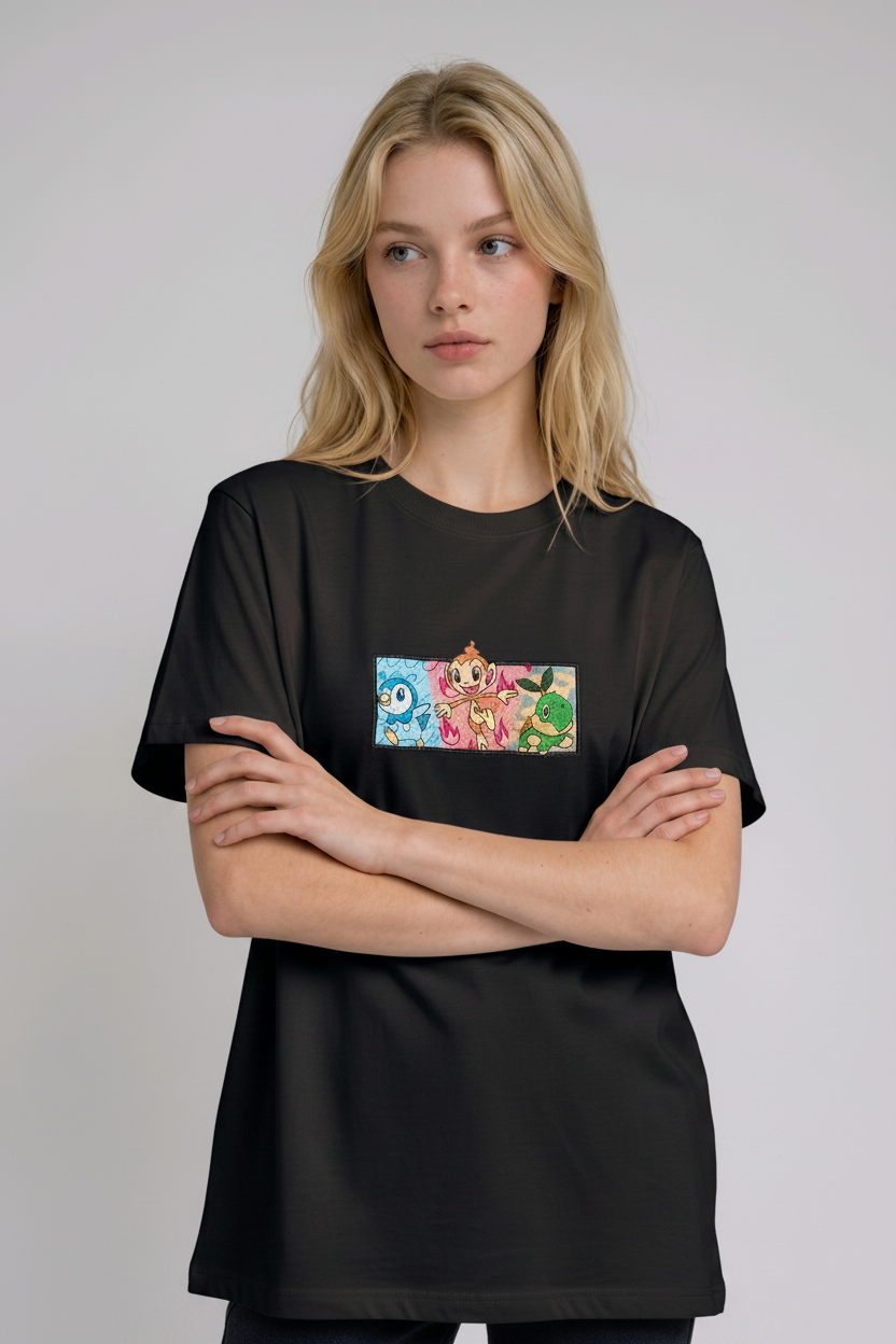 A young woman with wavy blonde hair standing against a plain grey studio background. She has her arms crossed and is wearing a black crew-neck t-shirt.

